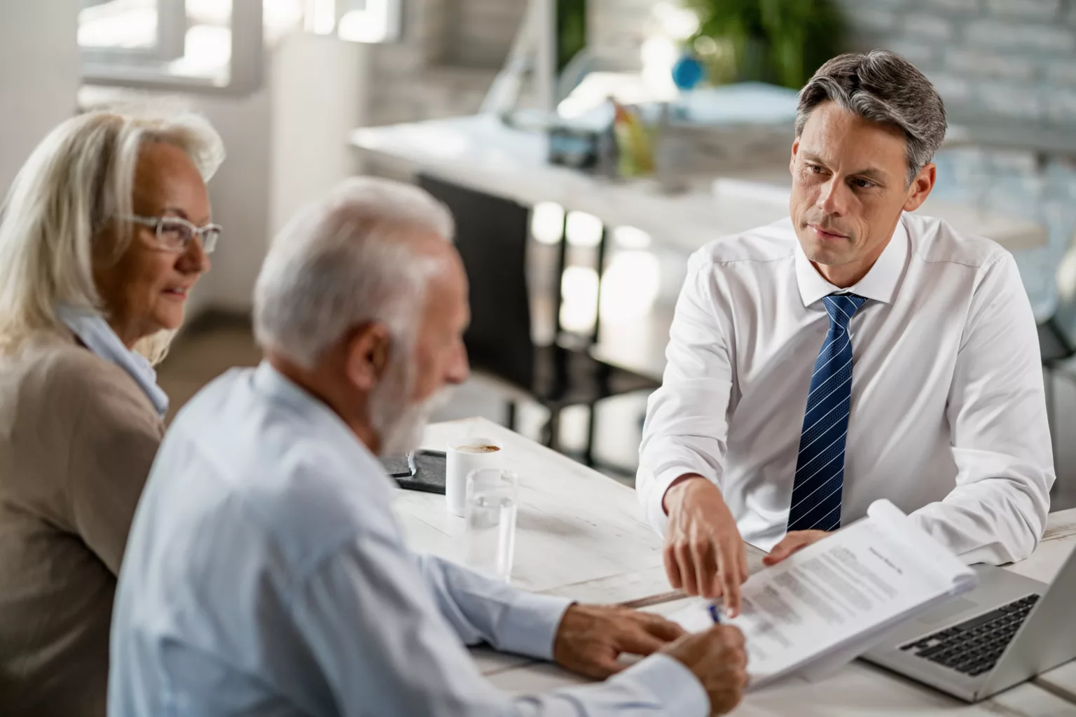 Bank manager having a meeting with senior couple and pointing at place they need to sign on the contract.