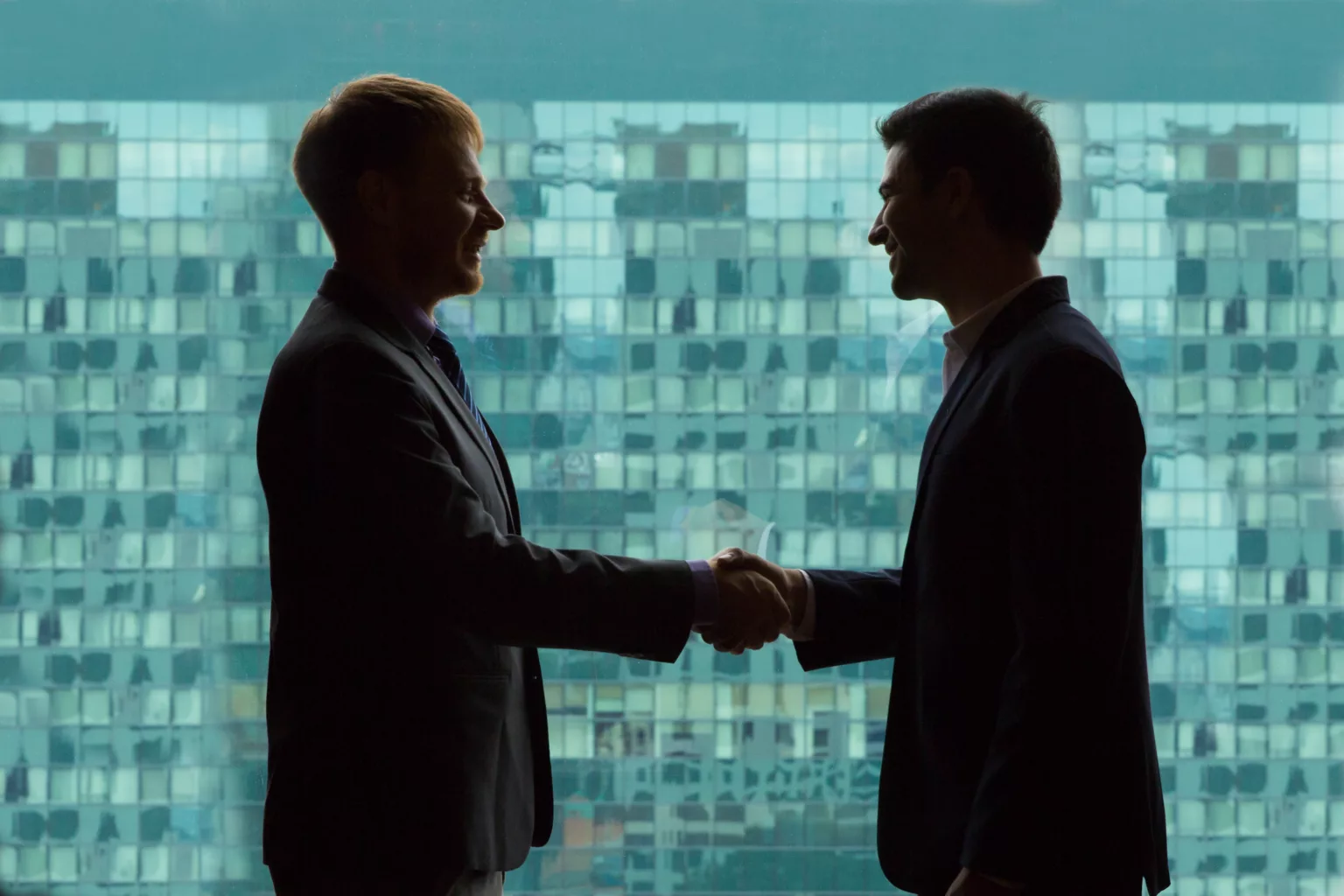 Silhouettes of businessmen shaking hands against big window in modern office building Silhouettes of businessmen shaking hands against big window in modern office building